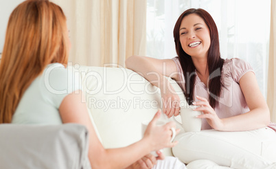 Smiling young women sitting on a sofa with cups