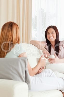 Chatting young women sitting on a sofa with cups