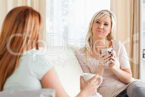 Cute young women sitting on a sofa with cups