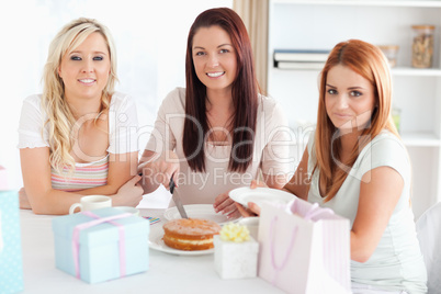 Smiling Women sitting at a table cutting a cake