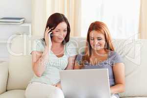 Charming Women sitting on a sofa with a laptop and a phone