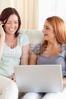 zwei Frauen sitzen mit Handy und Laptop auf Couch
