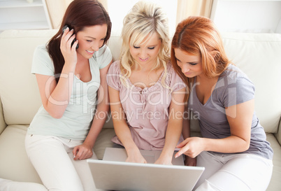 Freundinnen sitzen mit Handy und Laptop auf Couch
