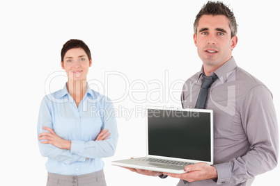 Office worker showing a laptop while his colleague is posing