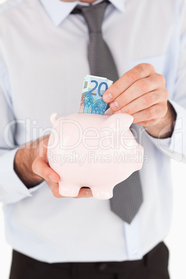 Close up of a man putting a bank note in a piggy bank