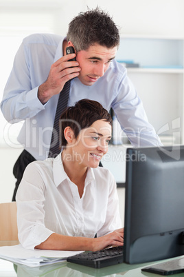 Man making a phone while looking at his colleague's screen