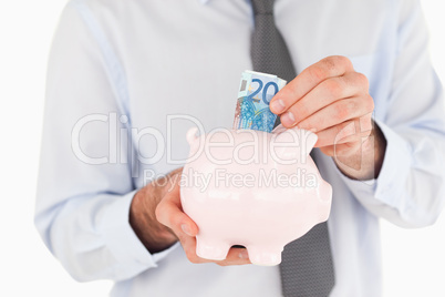 Close up hands putting a bank note in a piggy bank
