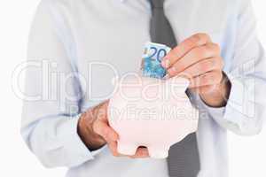 Close up hands putting a bank note in a piggy bank