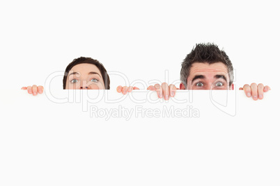 Man and woman hiding behind a white board with room for  copy sp
