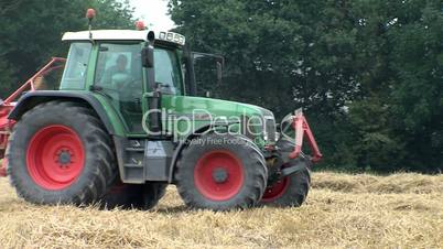 a red tractor machine is harvesting hay from wheat