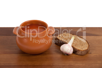 Borsch in ceramic pot with bread and garlic on wooden table