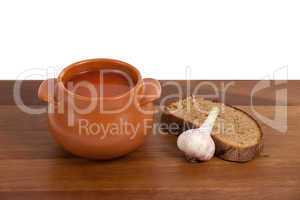 Borsch in ceramic pot with bread and garlic on wooden table
