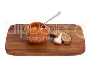 Soup in clay pot with bread and garlic on wooden kitchen board.