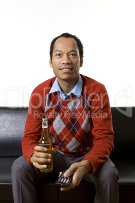 Smart casual business male sitting on couch drinking beer with remote in his hand