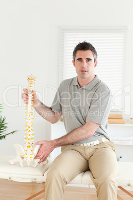 Chiropractor holding the model-spine looking into the camera