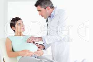 Doctor examining the woman's tummy with a stethoscope