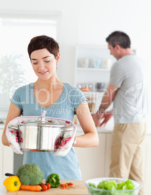 Cute wife holding a pot while her husband is washing the dishes