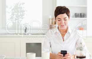 Young woman with mobile phone and coffee in kitchen