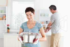 Cute Woman holding a pot while man is washing the dishes