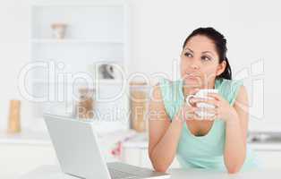 Thoughtful young woman with laptop and coffee