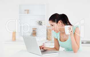 Young woman typing whilst holding a coffee