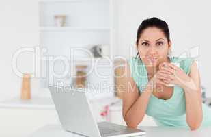 Young woman with coffee and laptop looking to camera