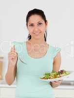 Young woman standing in kitchen with salad