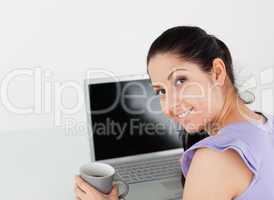 Cheerful young woman with coffee by laptop