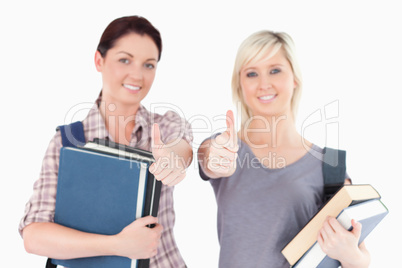 Two female students with books and thumbs up