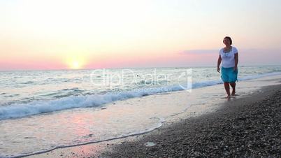 Woman walks on the beach at sunset