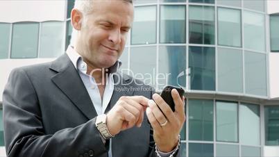 Businessman near office building sending email with cell phone