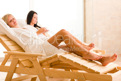 Luxury spa two women relax sitting sun-beds