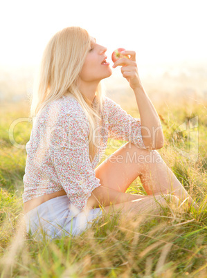 Girl is eating apple sitting on green field