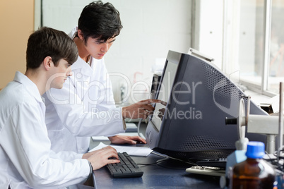 Chemist pointing at something on a monitor to his colleague