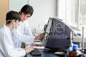 Chemist pointing at something on a monitor to his student