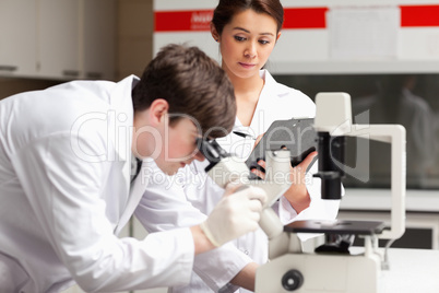 Science student looking in a microscope while his classmate is w
