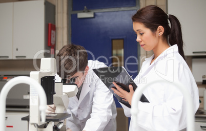 Science student looking in a microscope while his lecturer is wa