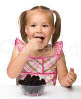 Cheerful little girl is eating blackberry