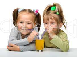 Two little girls are drinking orange juice