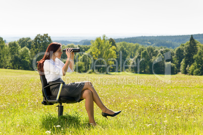 Businesswoman sit in sunny meadow seek binocular