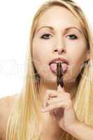 schöne blonde frau leckt an ihrem mit schokolade überzogenem finger