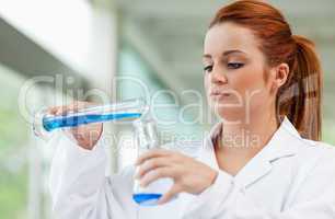 Young scientist pouring blue liquid in an Erlenmeyer flask