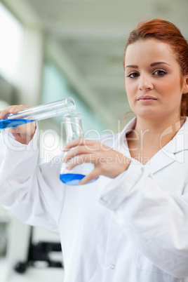 Portrait of a cute scientist pouring blue liquid in an Erlenmeye