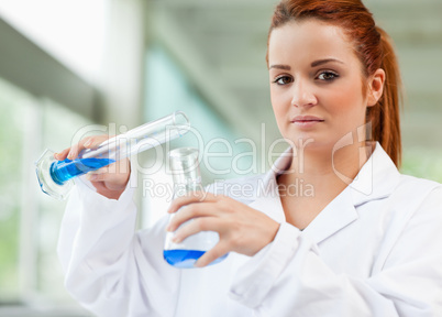 Cute scientist pouring blue liquid in an Erlenmeyer flask