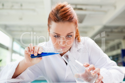 Beautiful serious scientist pouring liquid