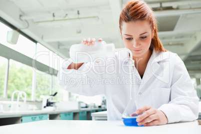 Red-haired focused scientist pouring liquid in a flask