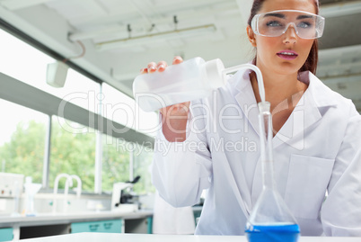 Female science student pouring liquid with protective glasses