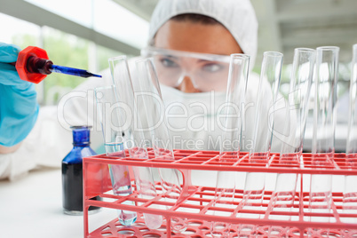 Protected female scientist dropping blue liquid in a test tube