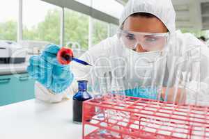 Protected cute female scientist dropping blue liquid in a test t