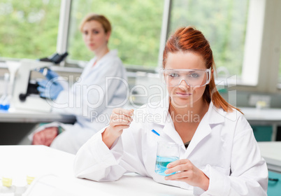 Scientist dropping liquid in a beaker while her colleague is usi